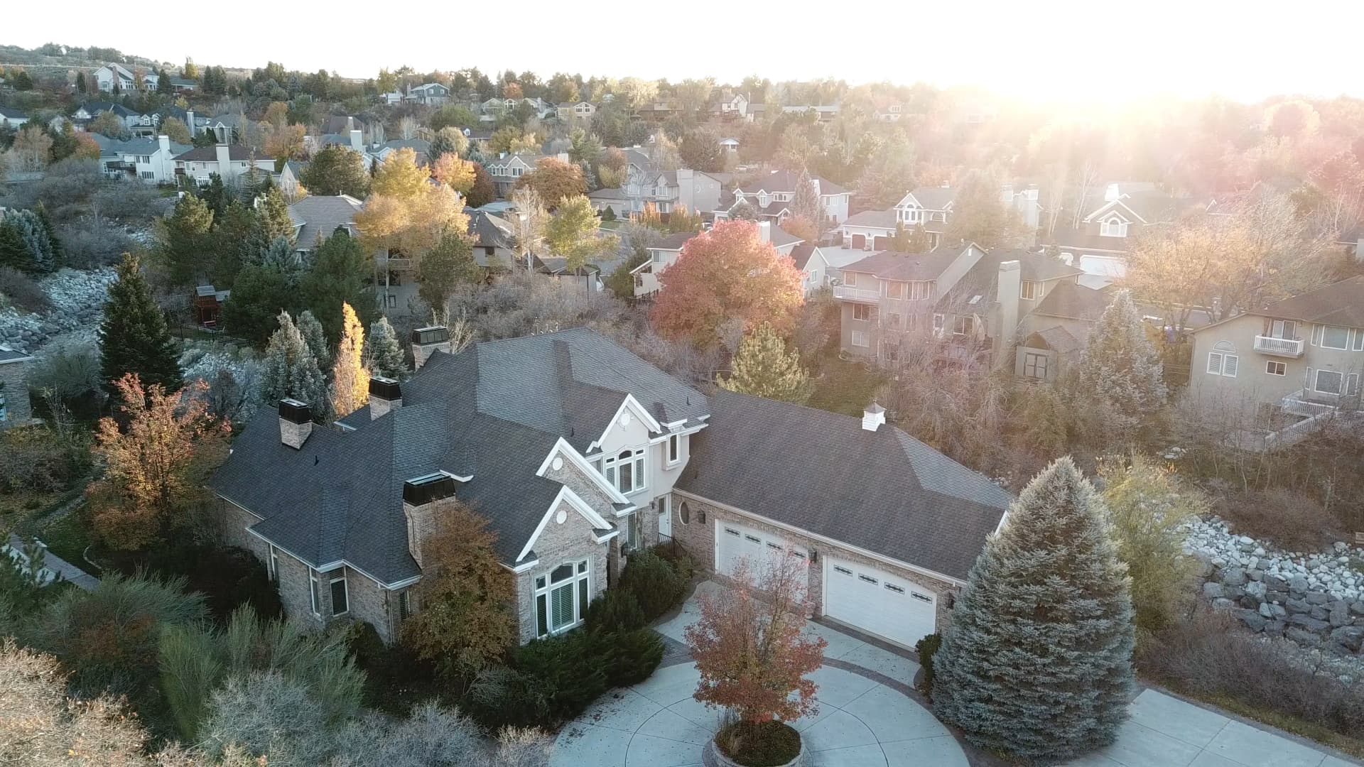 Aerial view of a stone home with a new dark shingle roof in a Northern Utah neighborhood